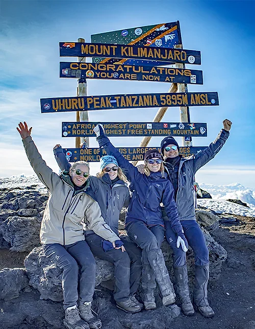 Familie sidder foran skiltet ved Uhuru Peak på toppen af Kilimanjaro