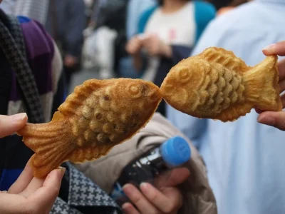 To personer holder taiyaki kager op, så det ligner fiskene kysser