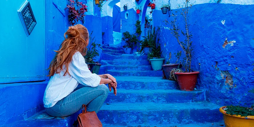 Kvinde sidder ved trappe i den blå by, Chefchaouen, i Marokko