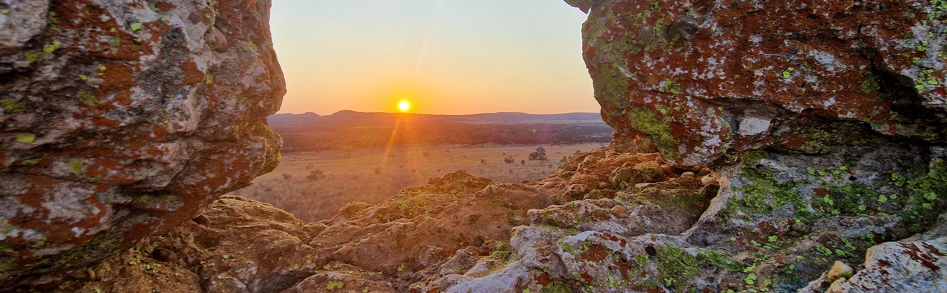 Solnedgang set gennem klipper over åbent landskab i Isalo Nationalpark