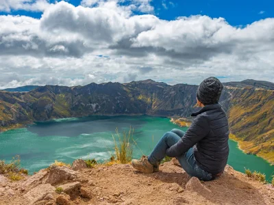 Kvinde sidder på kanten af kratersøen Quilotoa i Ecuador.