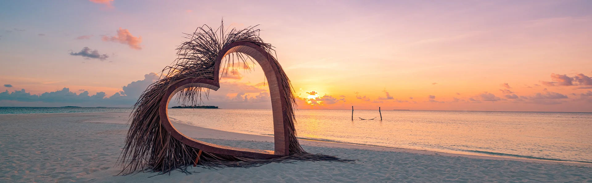 Skulptur af hjerte på en tropisk strand i solnedgangen