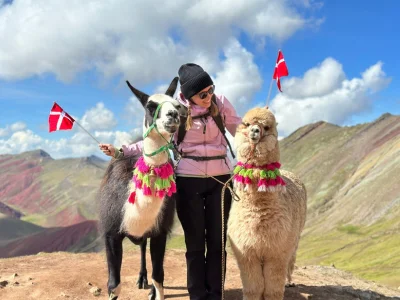 TourCompass-kollaga Iida står med to flag og alpaka på toppen af rainbow mountain i Peru.