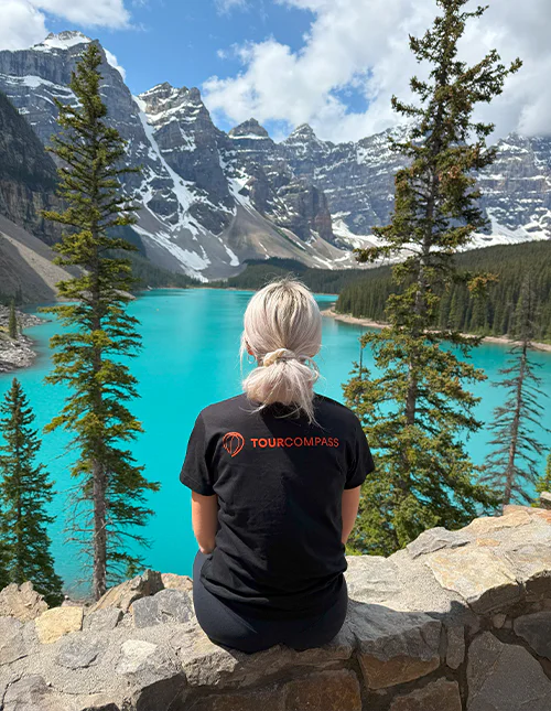 Kvinde med TourCompass t-shirt kigger ud over en turkisblå sø og sneklædte bjerge i Canada